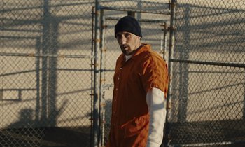 Movie still from “The Mustang” (2019), directed by Laure de Clermont-Tonnerre – A man in an orange jumpsuit standing in front of a fence; Medium shot, Low angle