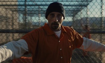 Movie still from “The Mustang” (2019), directed by Laure de Clermont-Tonnerre – A man in an orange shirt and black hat; Medium shot, Low angle