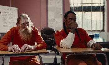 Movie still from “The Mustang” (2019), directed by Laure de Clermont-Tonnerre – A couple of men sitting at a table in a room; Medium shot, Over the shoulder angle