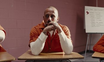 Movie still from “The Mustang” (2019), directed by Laure de Clermont-Tonnerre – A man sitting at a table with his hands under his chin; Medium shot, High angle