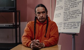 Movie still from “The Mustang” (2019), directed by Laure de Clermont-Tonnerre – A man sitting at a table with his hands crossed; Medium shot, Over the shoulder angle