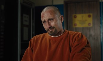 Movie still from “The Mustang” (2019), directed by Laure de Clermont-Tonnerre – A man with a shaved head wearing an orange sweatshirt; Close Up shot, Over the shoulder angle