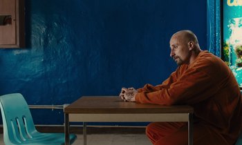 Movie still from “The Mustang” (2019), directed by Laure de Clermont-Tonnerre – A man sitting at a wooden table in an orange suit; Medium shot, Over the shoulder angle