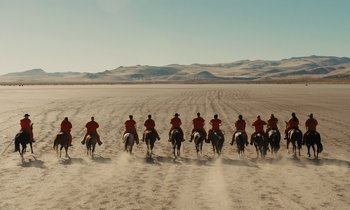 Movie still from “The Mustang” (2019), directed by Laure de Clermont-Tonnerre – A group of people riding horses on a dirt road; Extreme Wide shot, High angle