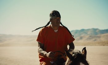 Movie still from “The Mustang” (2019), directed by Laure de Clermont-Tonnerre – A man in an orange shirt is on a horse; Medium shot, Over the shoulder angle