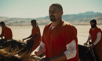 Movie still from “The Mustang” (2019), directed by Laure de Clermont-Tonnerre – A man in an orange shirt is riding a horse; Medium shot, Over the shoulder angle
