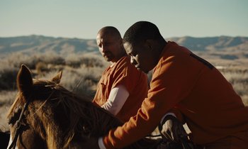Movie still from “The Mustang” (2019), directed by Laure de Clermont-Tonnerre – A couple of men are standing next to a horse; Medium shot, Over the shoulder angle