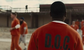 Movie still from “The Mustang” (2019), directed by Laure de Clermont-Tonnerre – A group of men in orange jumpsuits standing next to each other; Medium shot, Over the shoulder angle