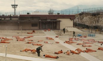 Movie still from “The Mustang” (2019), directed by Laure de Clermont-Tonnerre – A group of men in orange jumpsuits laying in the sand; Extreme Wide shot, High angle