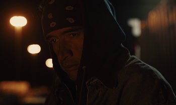 Movie still from “The Mustang” (2019), directed by Laure de Clermont-Tonnerre – A man wearing a hooded jacket in the dark with lights in the background; Close Up shot, Low angle