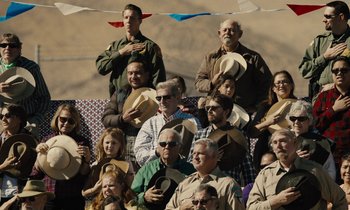 Movie still from “The Mustang” (2019), directed by Laure de Clermont-Tonnerre – A group of people standing in front of each other holding hats; Wide shot, High angle