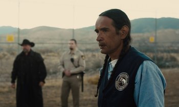 Movie still from “The Mustang” (2019), directed by Laure de Clermont-Tonnerre – A man in a blue vest standing next to two other men; Medium shot, Over the shoulder angle