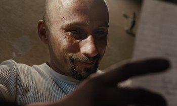 Movie still from “The Mustang” (2019), directed by Laure de Clermont-Tonnerre – A man with a shaved head looking at his cell phone; Close Up shot, High angle
