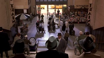 Movie still from “Naked Gun 33 1/3: The Final Insult” (1994), directed by Peter Segal – A group of people standing in an airport with luggage; Extreme Wide shot, High angle