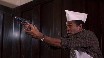 Movie still from “Naked Gun 33 1/3: The Final Insult” (1994), directed by Peter Segal – A man wearing a hat and holding a gun in his hand; Medium shot, Low angle
