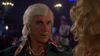 Movie still from “Naked Gun 33 1/3: The Final Insult” (1994), directed by Peter Segal – An older man with a long white hair and a colorful shirt is talking to a blonde woman; Close Up shot, Over the shoulder angle