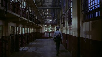 Movie still from “Naked Gun 33 1/3: The Final Insult” (1994), directed by Peter Segal – A man walking down a hallway in a jail cell; Wide shot, High angle