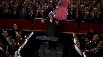 Movie still from “Naked Gun 33 1/3: The Final Insult” (1994), directed by Peter Segal – A man in a suit and bow tie standing in front of an orchestra; Wide shot, High angle