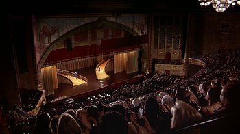 Movie still from “Naked Gun 33 1/3: The Final Insult” (1994), directed by Peter Segal – An audience is sitting in a large auditorium; Extreme Wide shot, High angle