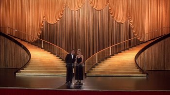 Movie still from “Naked Gun 33 1/3: The Final Insult” (1994), directed by Peter Segal – Two people standing in front of an empty stage; Extreme Wide shot, Low angle