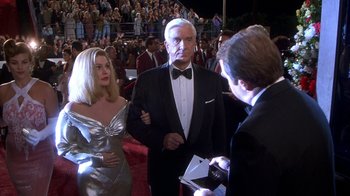 Movie still from “Naked Gun 33 1/3: The Final Insult” (1994), directed by Peter Segal – A man in a tuxedo talking to a woman in a silver dress; Medium shot, Over the shoulder angle