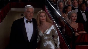 Movie still from “Naked Gun 33 1/3: The Final Insult” (1994), directed by Peter Segal – A man and a woman are standing in front of a staircase; Medium shot, Low angle