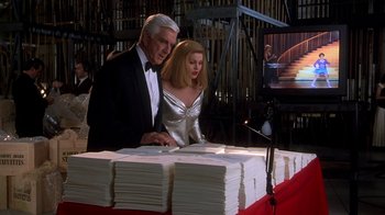 Movie still from “Naked Gun 33 1/3: The Final Insult” (1994), directed by Peter Segal – A man and a woman standing in front of stacks of papers; Medium shot, Low angle