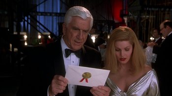 Movie still from “Naked Gun 33 1/3: The Final Insult” (1994), directed by Peter Segal – A man and a woman looking at an envelope; Close Up shot, Low angle