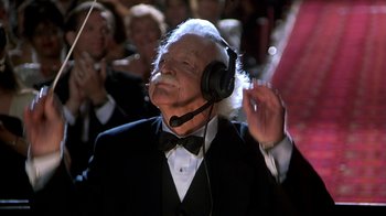 Movie still from “Naked Gun 33 1/3: The Final Insult” (1994), directed by Peter Segal – An older man wearing a black bow tie and headphones; Medium shot, Low angle