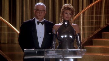 Movie still from “Naked Gun 33 1/3: The Final Insult” (1994), directed by Peter Segal – A man and a woman standing next to each other at a podium; Medium shot, Low angle