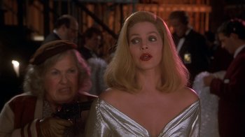 Movie still from “Naked Gun 33 1/3: The Final Insult” (1994), directed by Peter Segal – A woman in a silver dress standing next to another woman in a crowd of onlookers; Medium shot, Over the shoulder angle