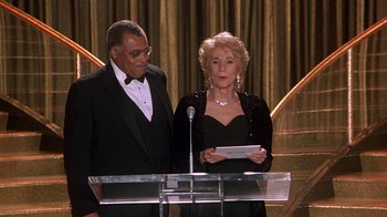 Movie still from “Naked Gun 33 1/3: The Final Insult” (1994), directed by Peter Segal – A man and a woman standing in front of a microphone; Medium shot, Low angle