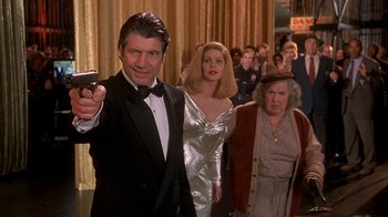 Movie still from “Naked Gun 33 1/3: The Final Insult” (1994), directed by Peter Segal – A man in a tuxedo holding up a cell phone; Medium shot, Low angle