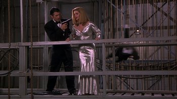 Movie still from “Naked Gun 33 1/3: The Final Insult” (1994), directed by Peter Segal – A man and a woman standing next to each other in front of a metal fence; Medium shot, Low angle