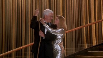 Movie still from “Naked Gun 33 1/3: The Final Insult” (1994), directed by Peter Segal – A man and a woman dancing in front of a gold curtain; Medium shot, Low angle
