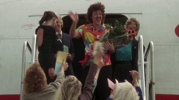 Movie still from “The Naked Gun: From the Files of Police Squad!” (1988), directed by David Zucker – A group of people standing next to each other holding flowers; Medium shot, Over the shoulder angle