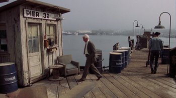 Movie still from “The Naked Gun: From the Files of Police Squad!” (1988), directed by David Zucker – An older man in a suit and tie walking on a dock; Wide shot, High angle