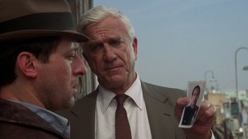 Movie still from “The Naked Gun: From the Files of Police Squad!” (1988), directed by David Zucker – A man in a suit and a hat looking at another man in a suit and a hat; Close Up shot, Over the shoulder angle