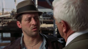Movie still from “The Naked Gun: From the Files of Police Squad!” (1988), directed by David Zucker – A man wearing a hat talking to another man; Close Up shot, Over the shoulder angle