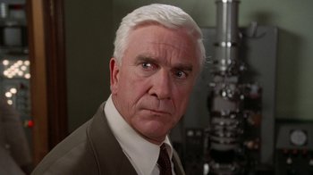 Movie still from “The Naked Gun: From the Files of Police Squad!” (1988), directed by David Zucker – An older man in a suit and tie looking at the camera; Close Up shot, High angle