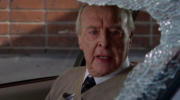 Movie still from “The Naked Gun: From the Files of Police Squad!” (1988), directed by David Zucker – An older man wearing a suit and tie in the back of a car; Close Up shot, Over the shoulder angle