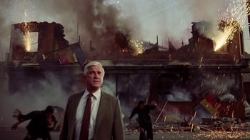 Movie still from “The Naked Gun: From the Files of Police Squad!” (1988), directed by David Zucker – An older man standing in front of an explosion; Medium shot, Low angle