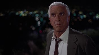 Movie still from “The Naked Gun: From the Files of Police Squad!” (1988), directed by David Zucker – An older man in a suit and tie looking at the camera; Close Up shot, Over the shoulder angle