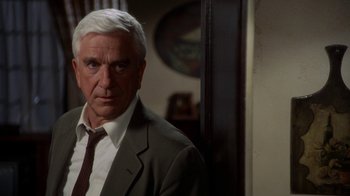 Movie still from “The Naked Gun: From the Files of Police Squad!” (1988), directed by David Zucker – An older man wearing a suit and tie in a room; Close Up shot, Over the shoulder angle