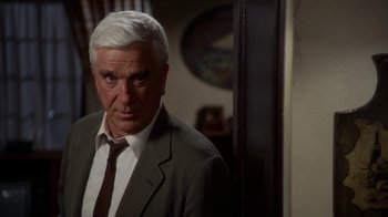 Movie still from “The Naked Gun: From the Files of Police Squad!” (1988), directed by David Zucker – An older man wearing a suit and tie in front of a mirror; Close Up shot, Over the shoulder angle