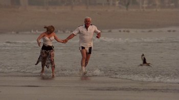 Movie still from “The Naked Gun: From the Files of Police Squad!” (1988), directed by David Zucker – A man and a woman holding hands while walking in the ocean; Wide shot, High angle