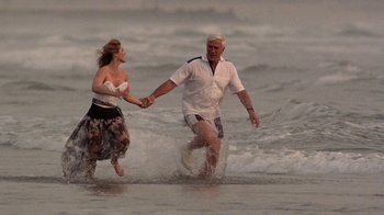 Movie still from “The Naked Gun: From the Files of Police Squad!” (1988), directed by David Zucker – An older man and a younger woman are running through the water; Wide shot, High angle