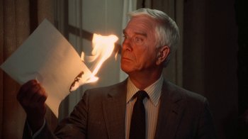 Movie still from “The Naked Gun: From the Files of Police Squad!” (1988), directed by David Zucker – An older man in a suit and tie looking at a paper; Close Up shot, Low angle