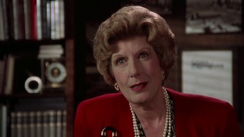 Movie still from “The Naked Gun: From the Files of Police Squad!” (1988), directed by David Zucker – An older woman wearing a red jacket and a pearl necklace; Close Up shot, Over the shoulder angle