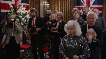 Movie still from “The Naked Gun: From the Files of Police Squad!” (1988), directed by David Zucker – A group of people taking pictures in a room; Medium shot, High angle